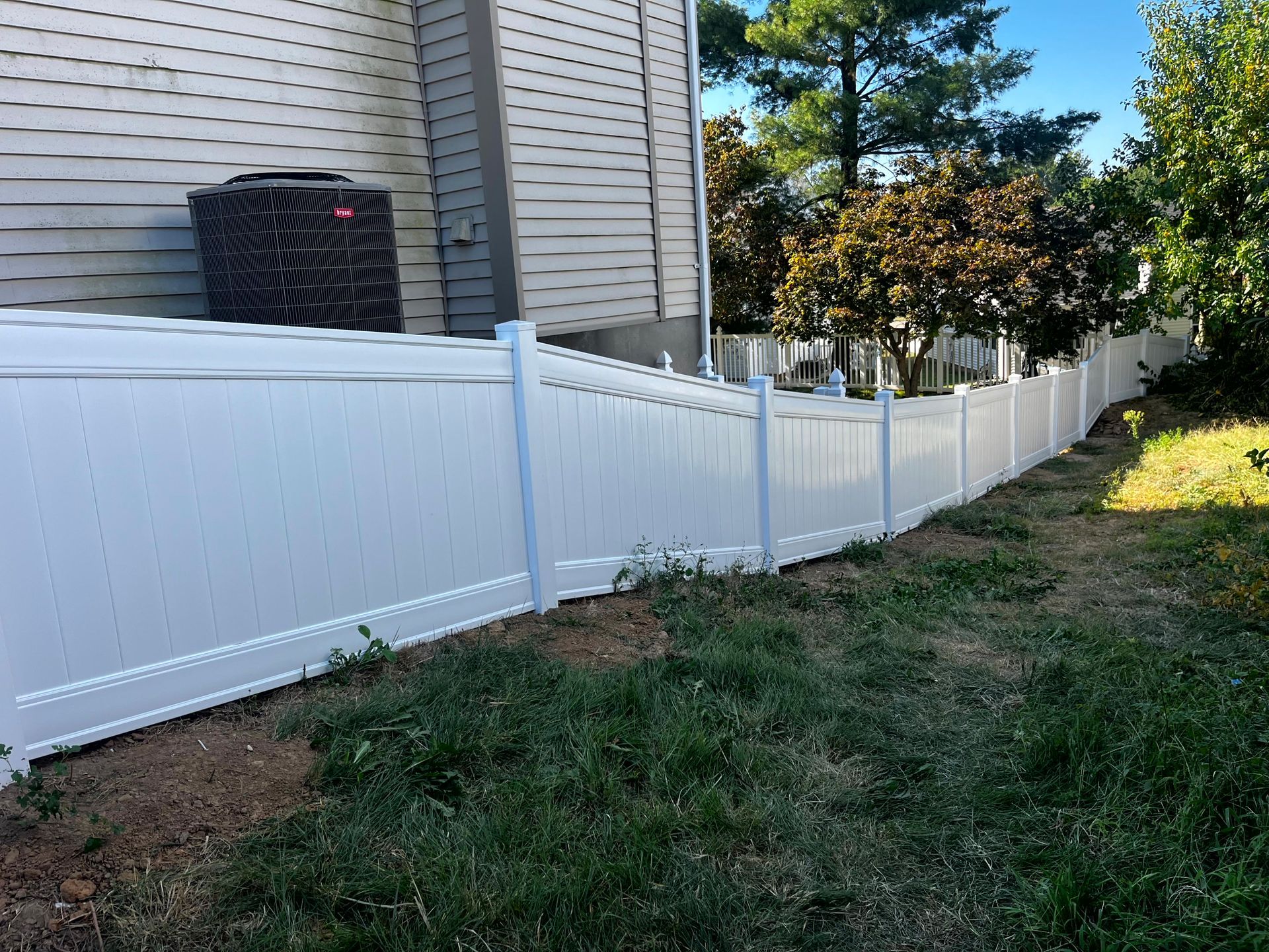 White vinyl fence along a grassy yard, beside a house with an air conditioning unit.
