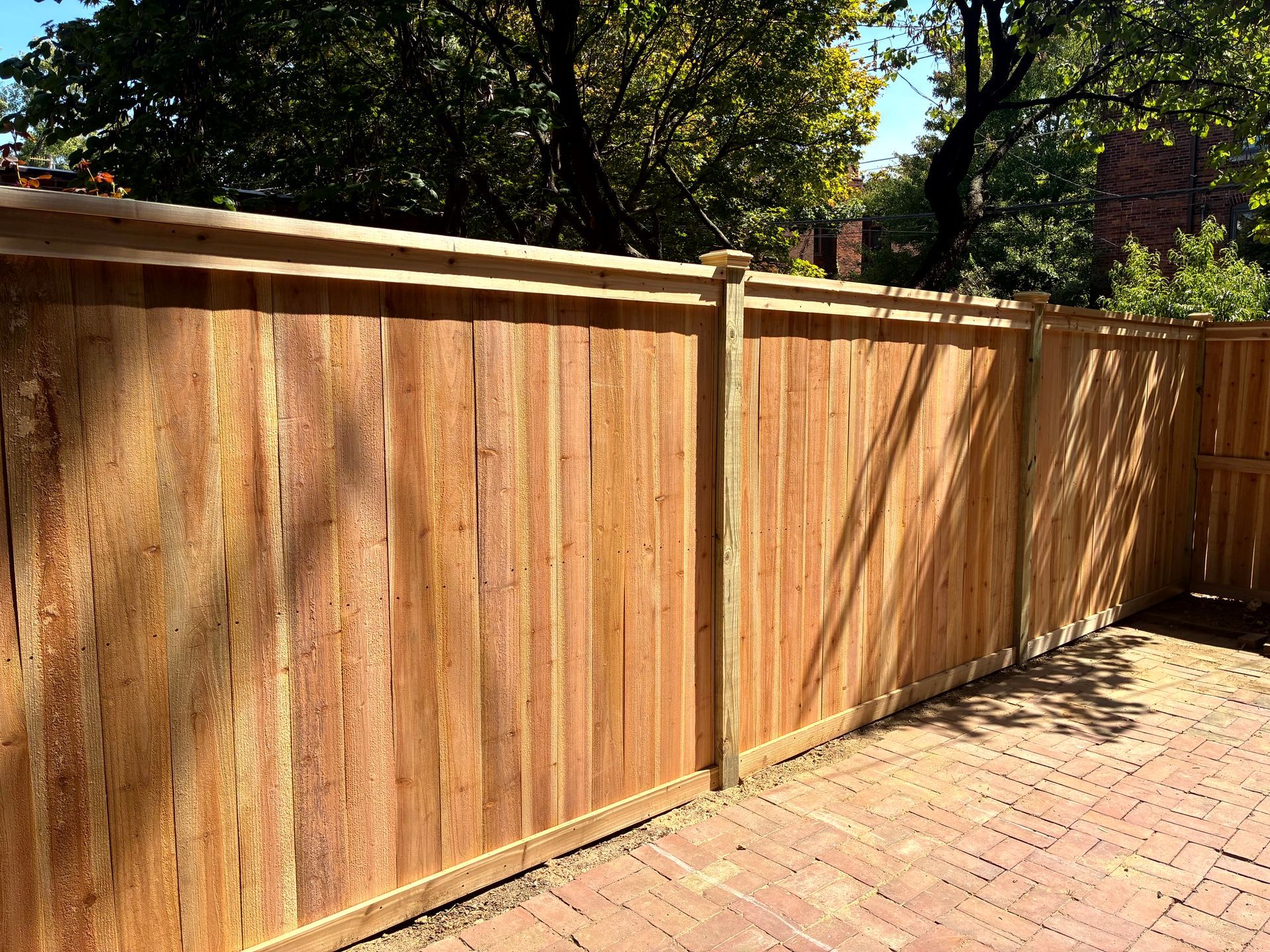 Wooden privacy fence on brick patio, trees in background.