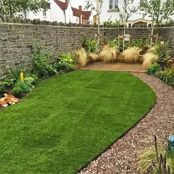 Curved green lawn bordered by gravel and plants in a walled garden