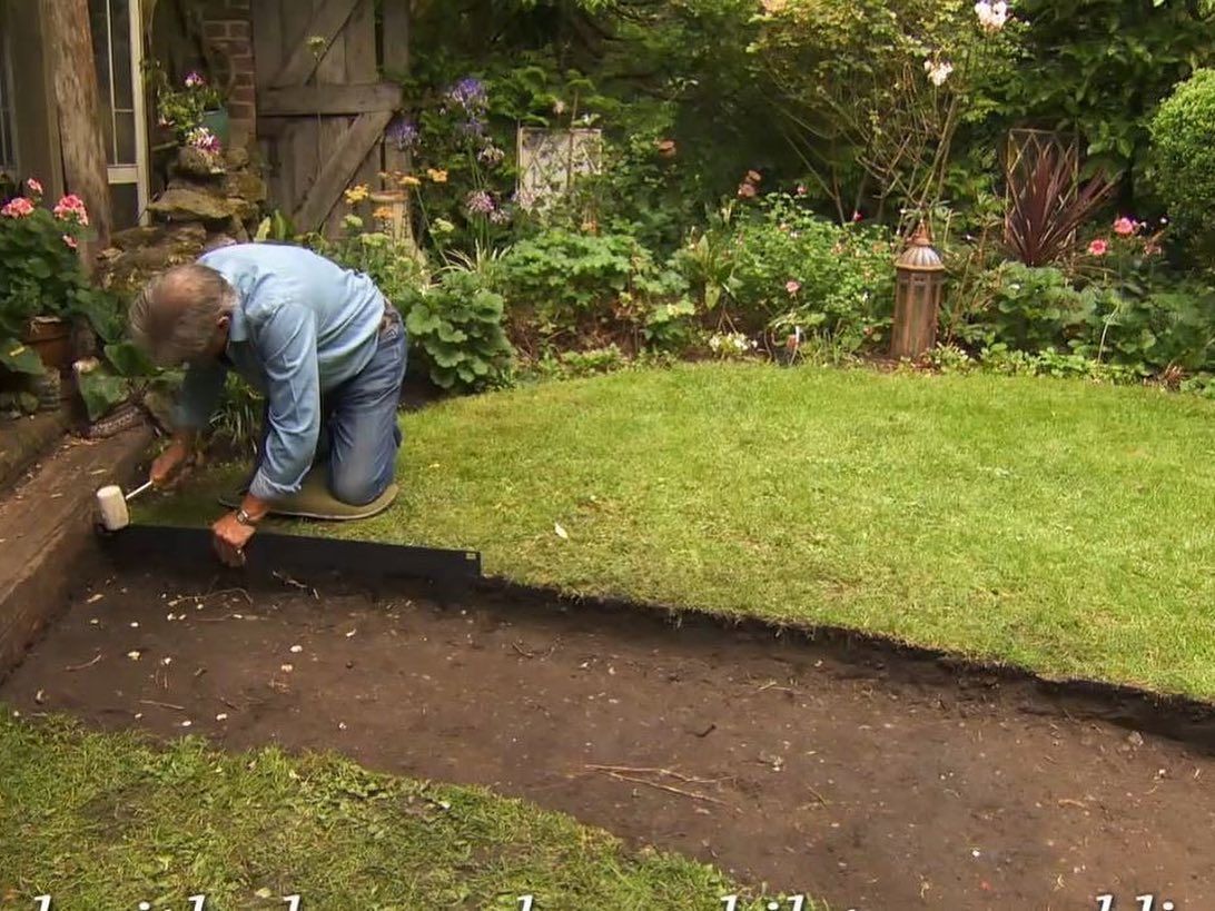 Person laying edging along a garden path beside a green lawn and flowers