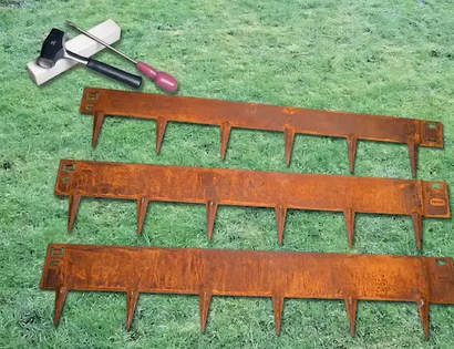 Three rusty metal rake tines laid on green grass beside a garden trowel and brush
