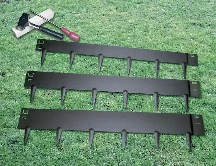 Three black metal garden edging panels and a hand tool laid on grass.