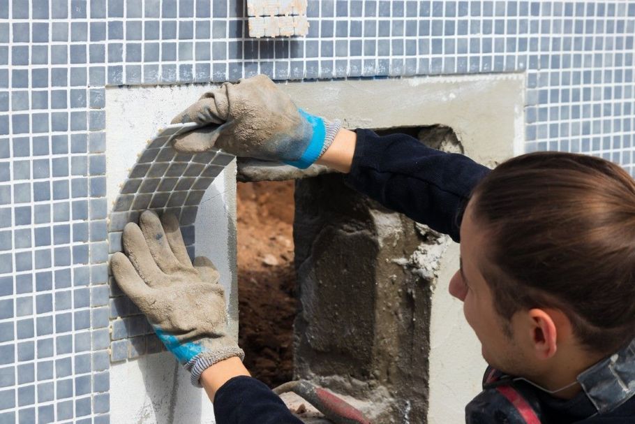 Worker fitting gray tiles around a wall opening with gloved hands
