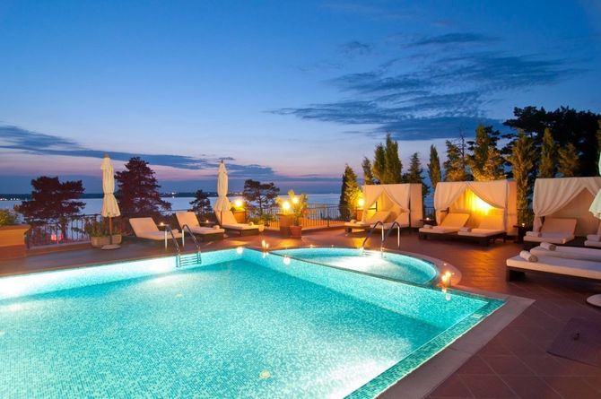 Luxury resort pool at dusk with turquoise water, lounge chairs, and cabanas overlooking the sea