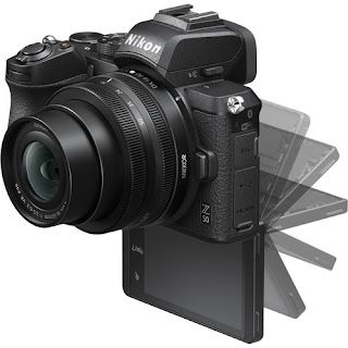 A black nikon camera is sitting on a white surface. There is an afterimage affect of the video finder screen opening downward as if to indicate motion.
