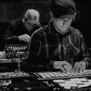 A man is sitting at a table playing a keyboard or soundboard in a black and white photo.