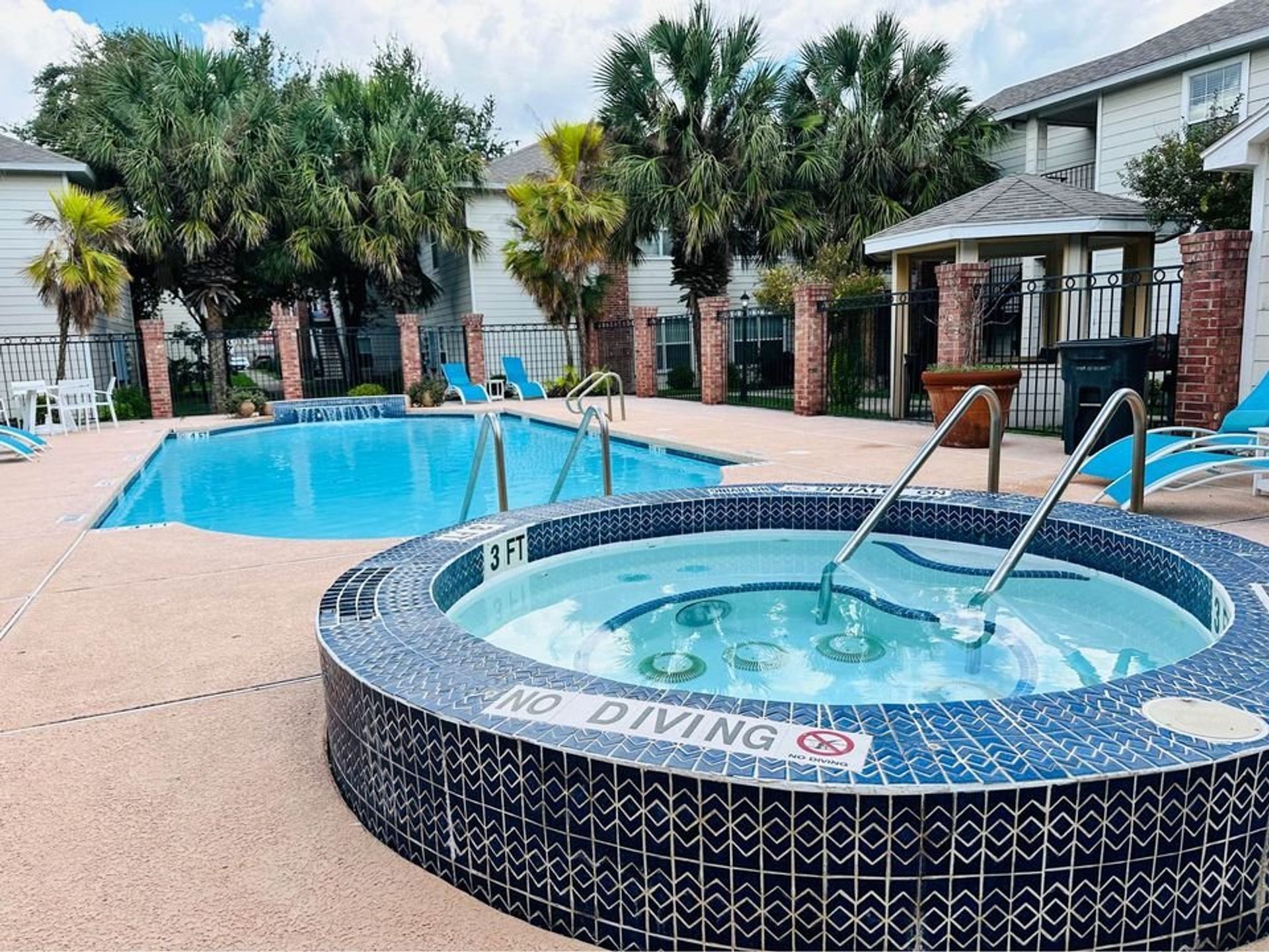 Apartment pool with spa, palm trees, and lounge chairs on a sunny day
