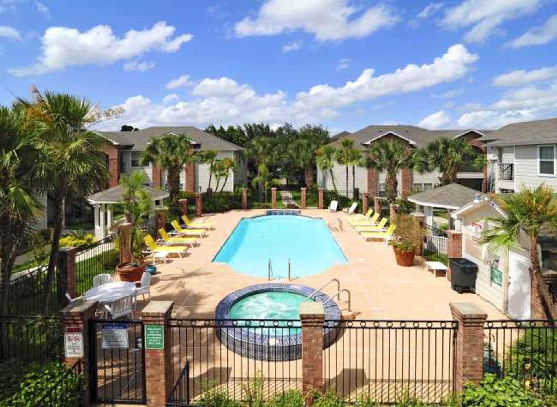 Apartment courtyard with a turquoise pool, hot tub, lounge chairs, and palm trees under a blue sky
