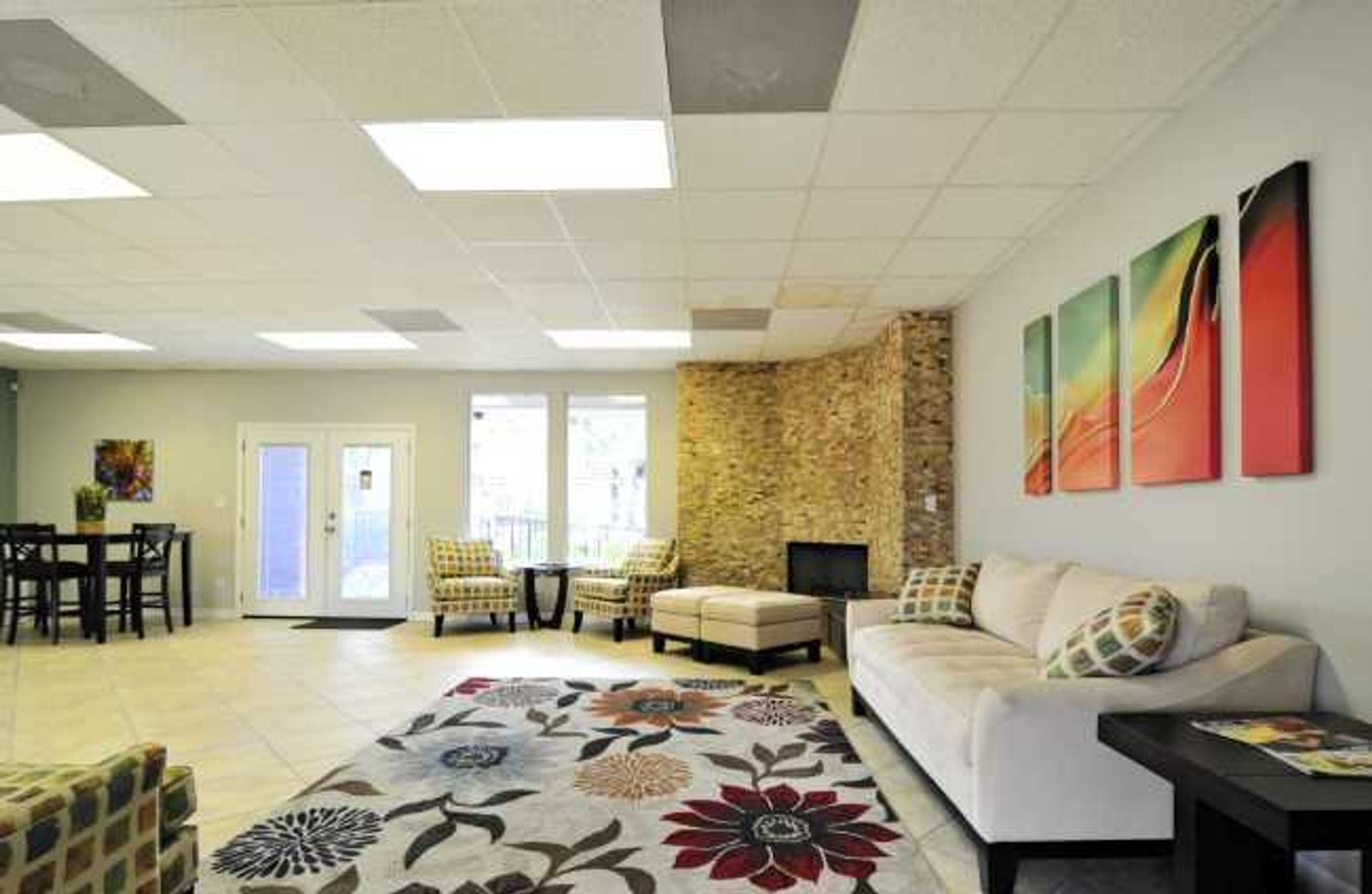 Spacious lounge with sofas, floral rug, tables, and colorful wall art under bright ceiling lights