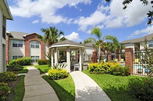 Landscaped apartment courtyard with walkway, gazebo, palm trees, and blue sky