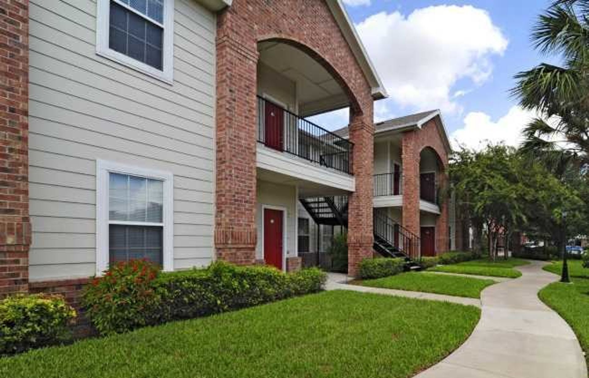 Apartment building with red brick and beige siding beside a curved walkway and green lawn