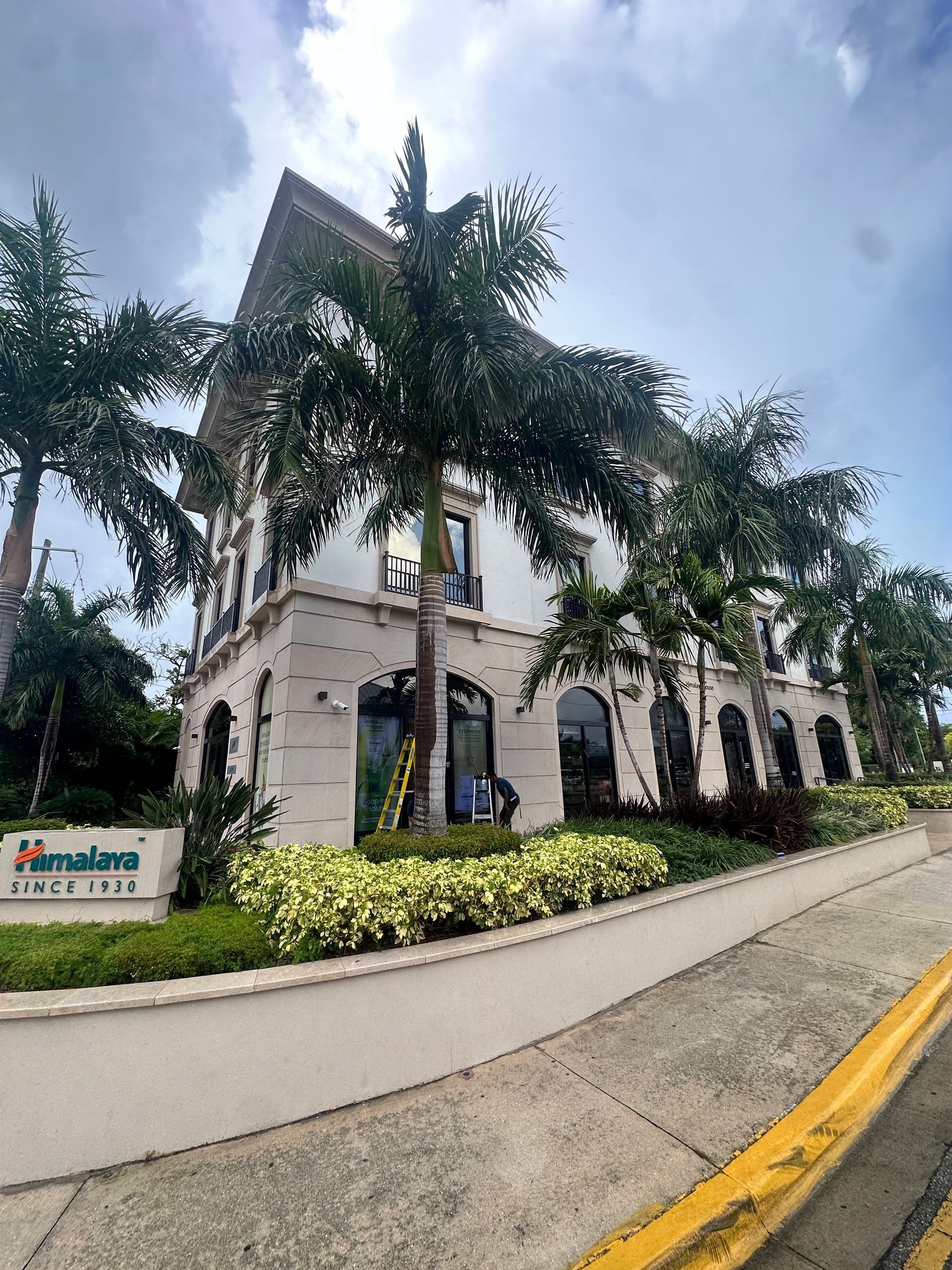 Cream-colored building with arched windows, palm trees, and a sign that reads 