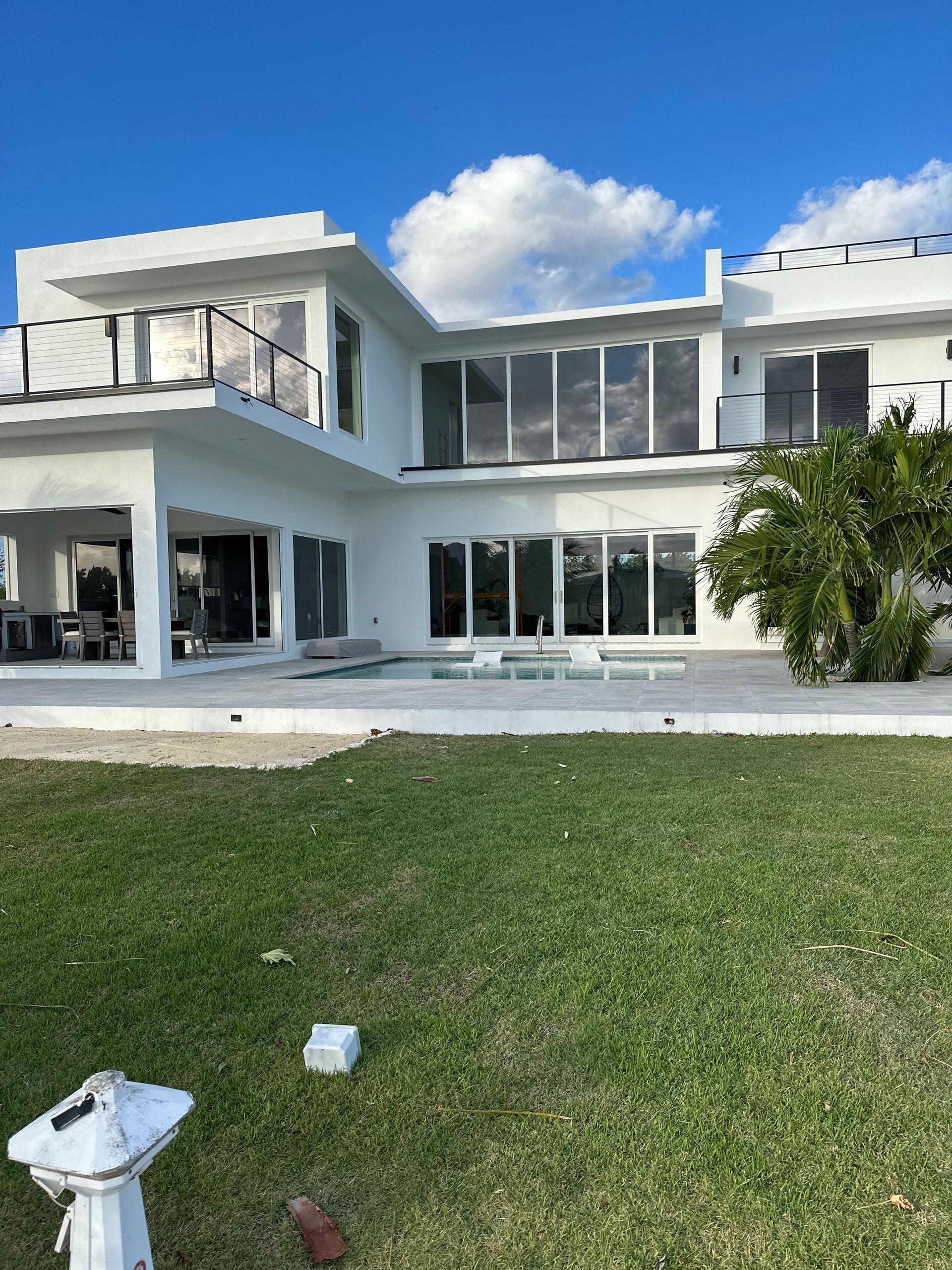 White modern house with large windows, patio, and green lawn under a blue sky.