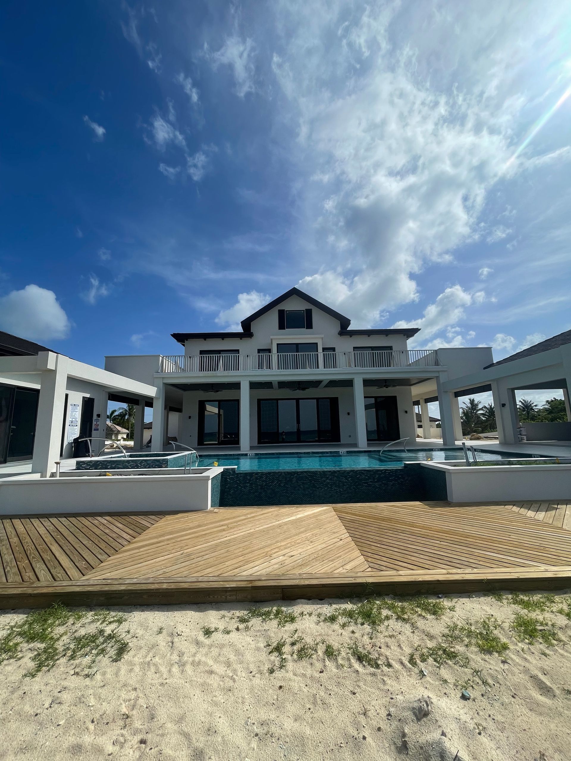 Luxurious white house with a pool, blue sky, and sun glare.