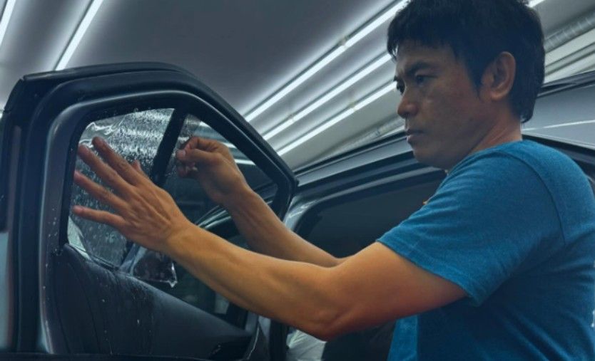 A person applying window tint to a car window in a garage.