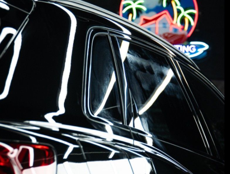 Black car with reflective surfaces and neon sign in background.