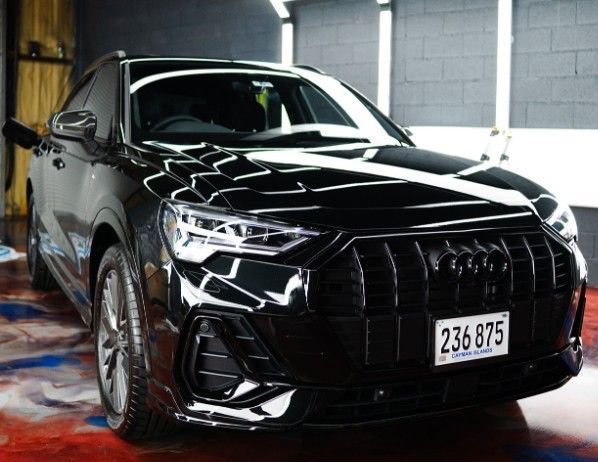 Black Audi Q3 SUV with shiny, wet finish, parked in a car detailing bay.