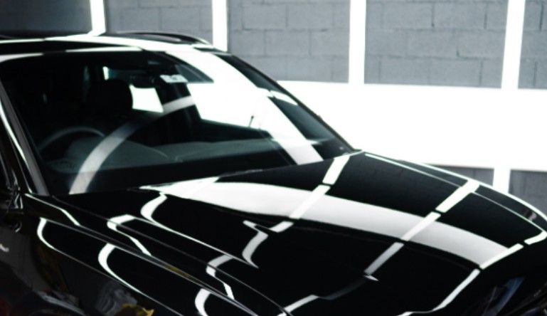 Black car reflecting bright lights in a studio setting.