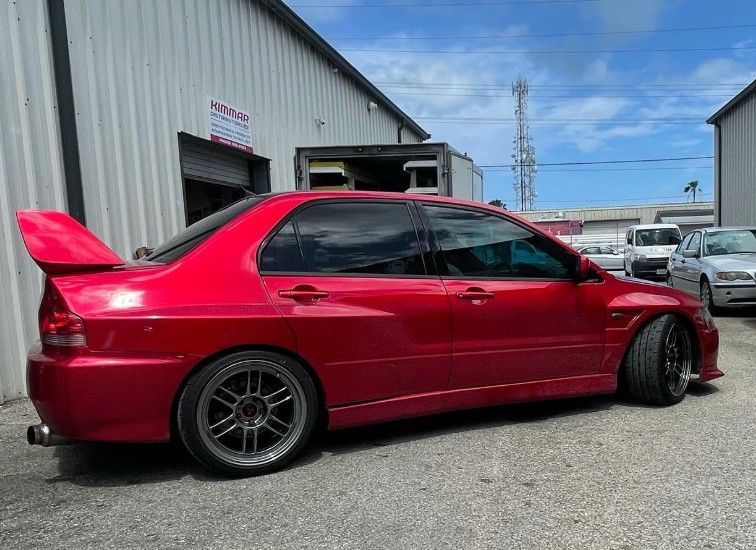 Red Mitsubishi Lancer Evolution parked outside a building, tinted windows, dark wheels, and large spoiler.