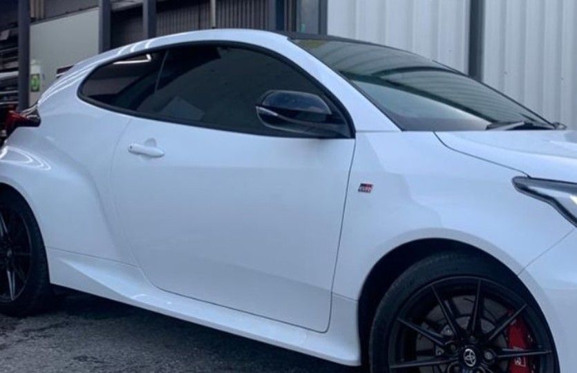 White Toyota GR Yaris sports car with black wheels and red brake calipers parked outside.