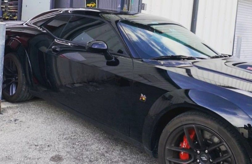 Black Dodge Challenger with red brake calipers parked in front of a building.