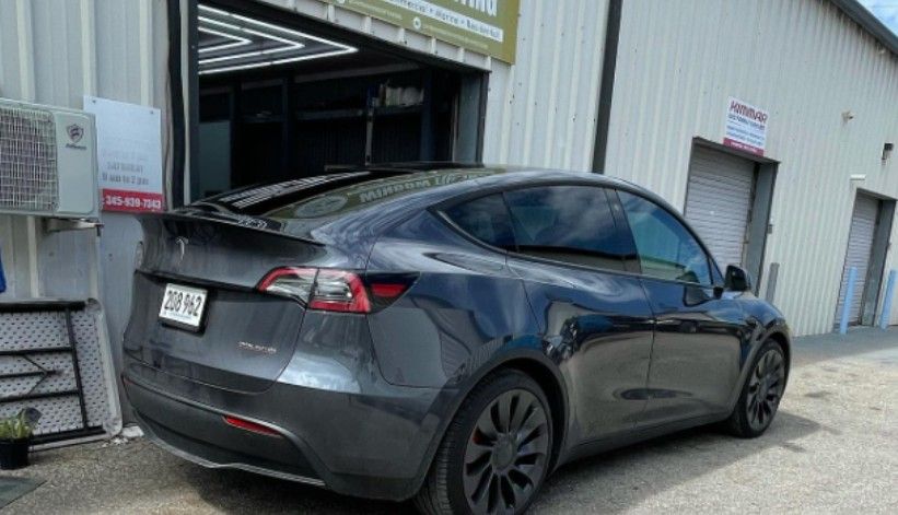 Dark gray Tesla Model Y parked outside a garage.