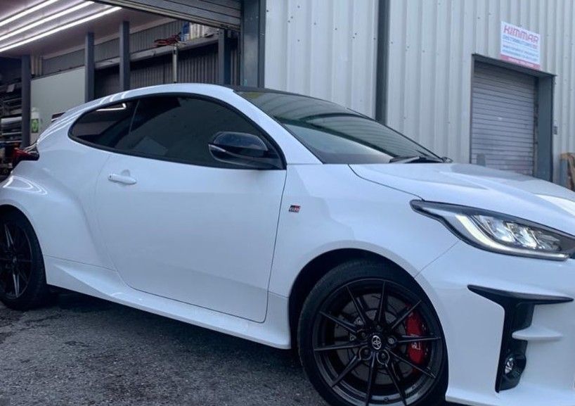 White Tesla Model Y parked in front of a building with black rims and a black roof.