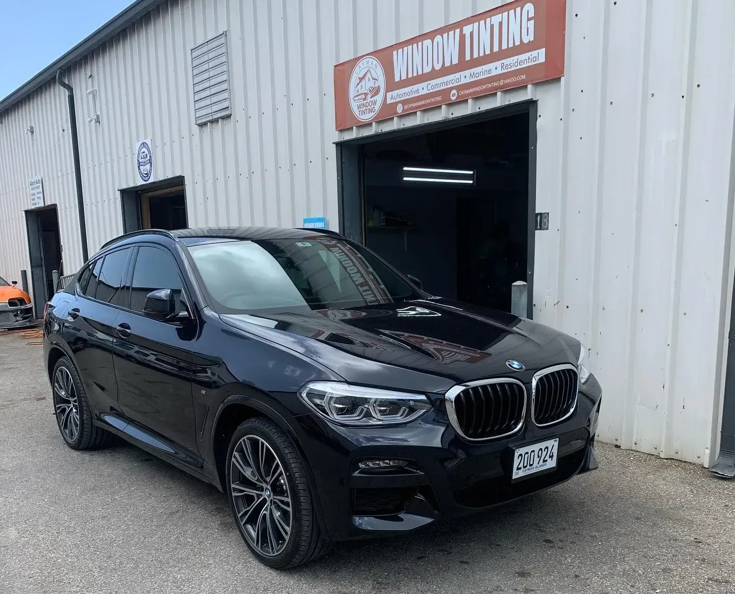 Black BMW X4 with tinted windows parked in front of a window tinting shop.