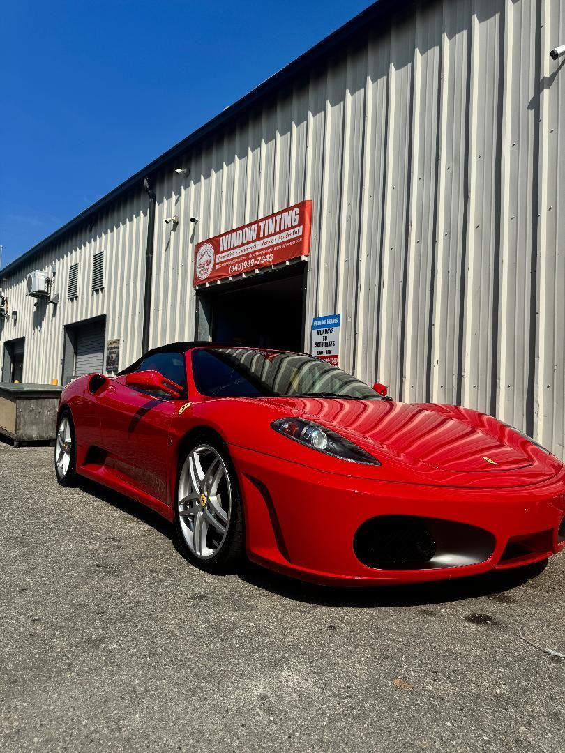 Red Ferrari sports car parked in front of a garage under a blue sky.