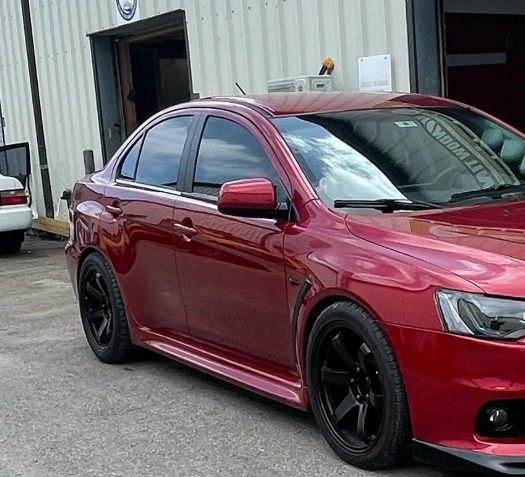 Red sporty sedan with black rims parked outside a garage