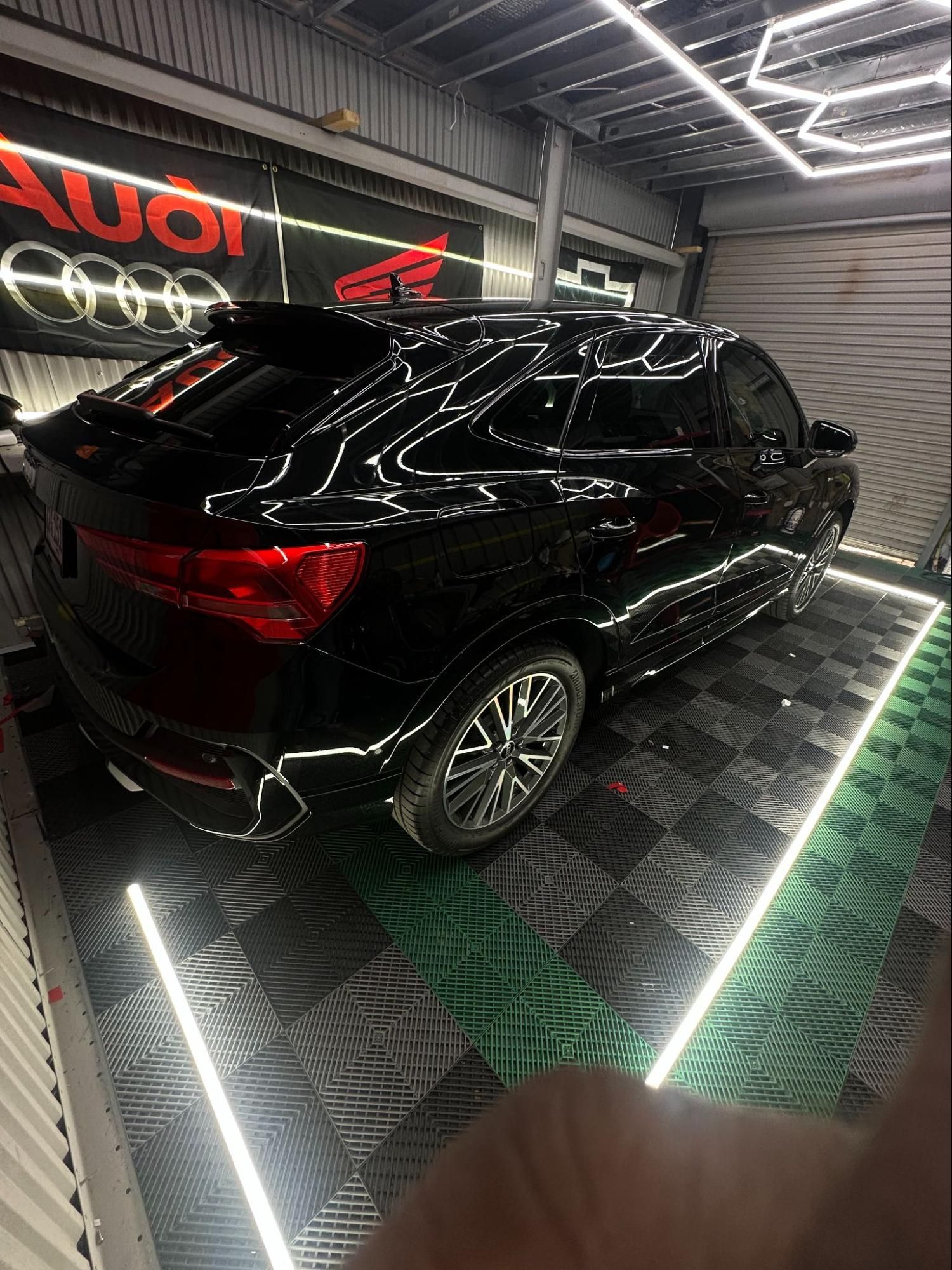 Black Audi SUV in a service bay, with bright overhead and floor lighting.