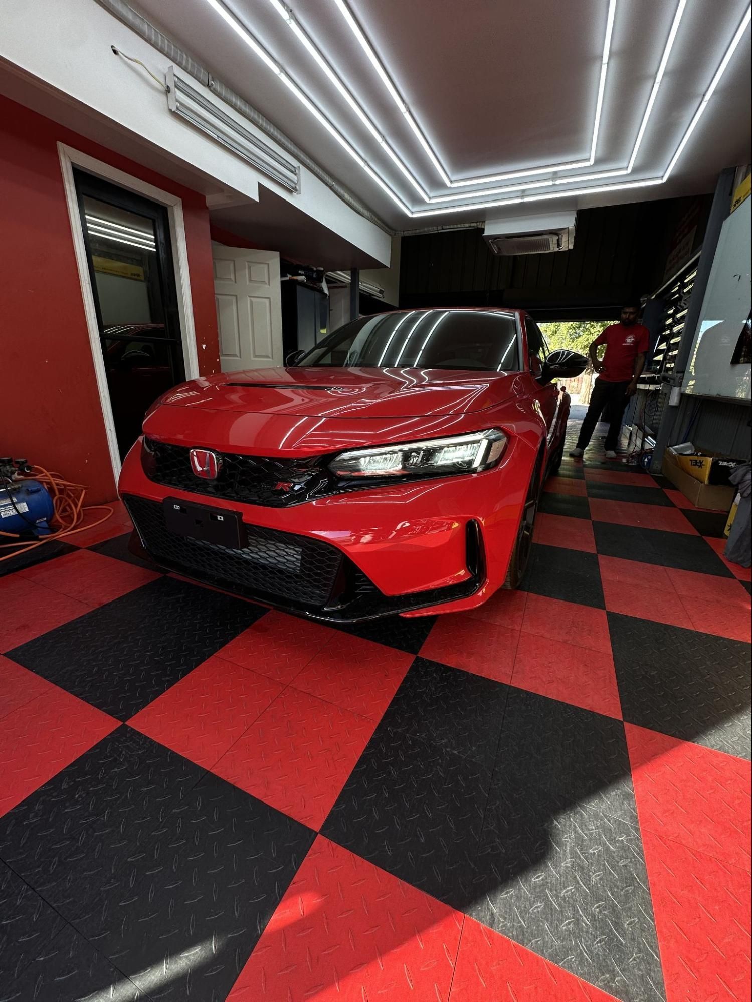 A red car is parked in a garage with a checkered floor.