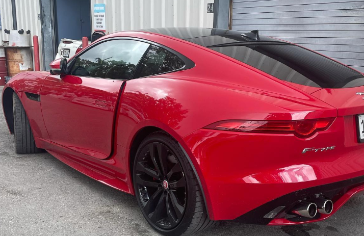 Red sports coupe parked beside a corrugated metal building, rear three-quarter view