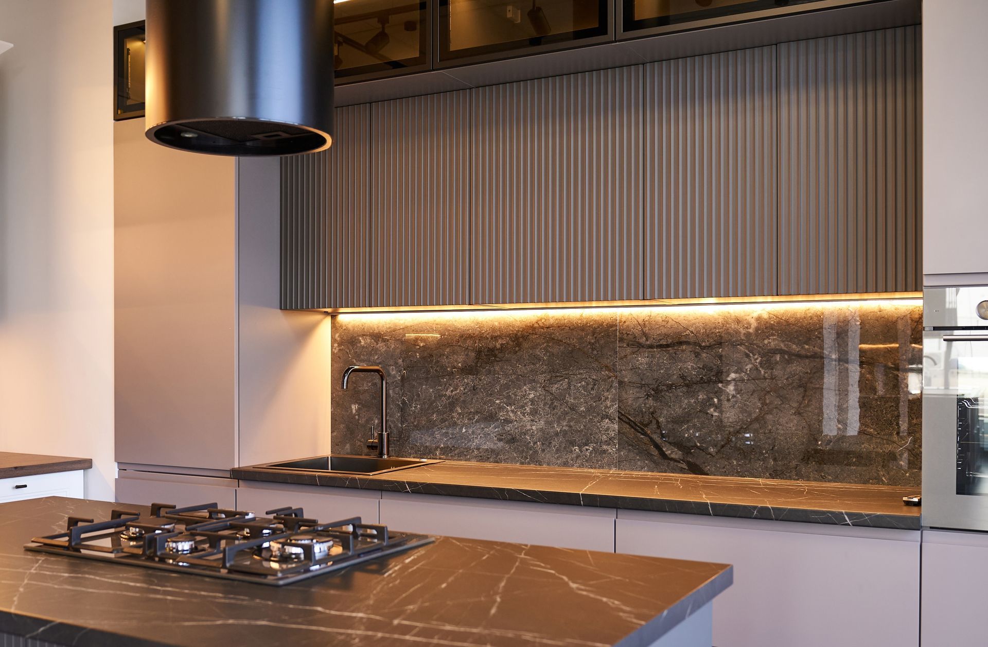 Modern kitchen with gas cooktop, marble island, and wood slat backsplash with under-cabinet lighting
