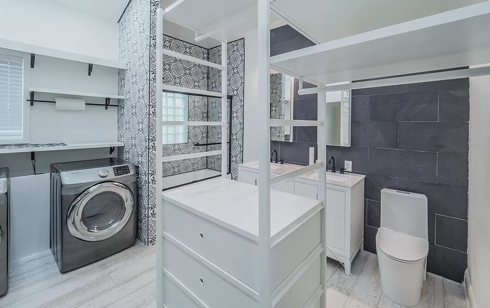 Laundry room with washer, storage, sink, and toilet; white and grey color scheme.