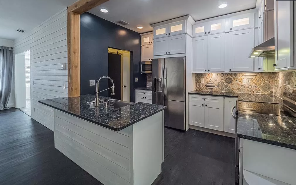 Modern kitchen with white cabinets, stainless steel appliances, dark granite countertops, and dark wood floors.