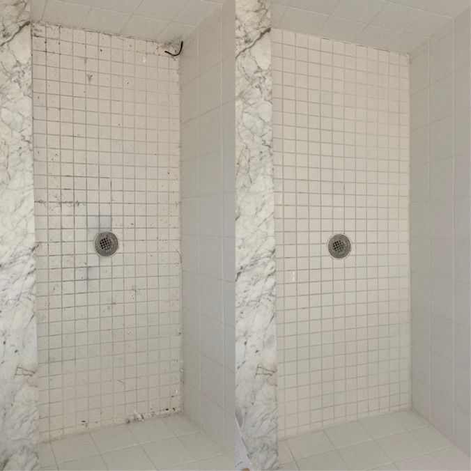 Before and after of a cleaned white tiled shower with marble accents; shower head and drain visible.