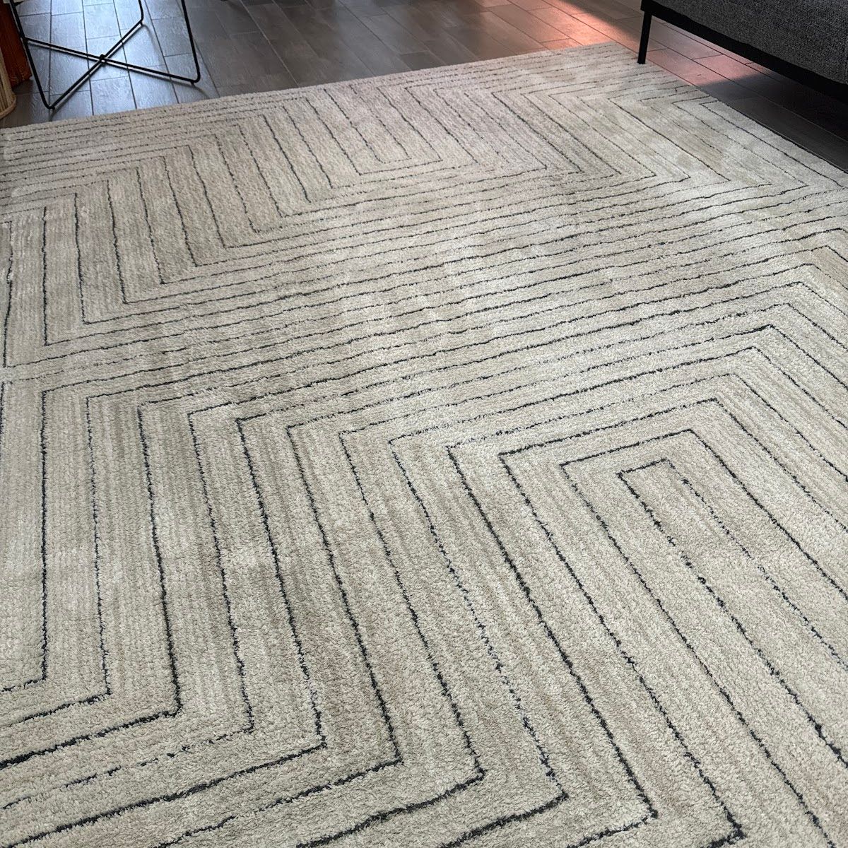 Beige rug with geometric black line pattern on a wood floor.