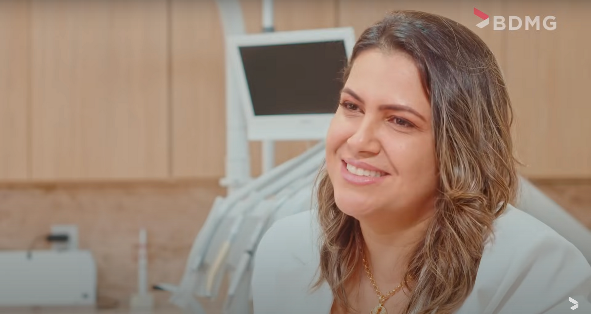 Uma mulher sorri sentada em uma cadeira odontológica em um consultório odontológico.