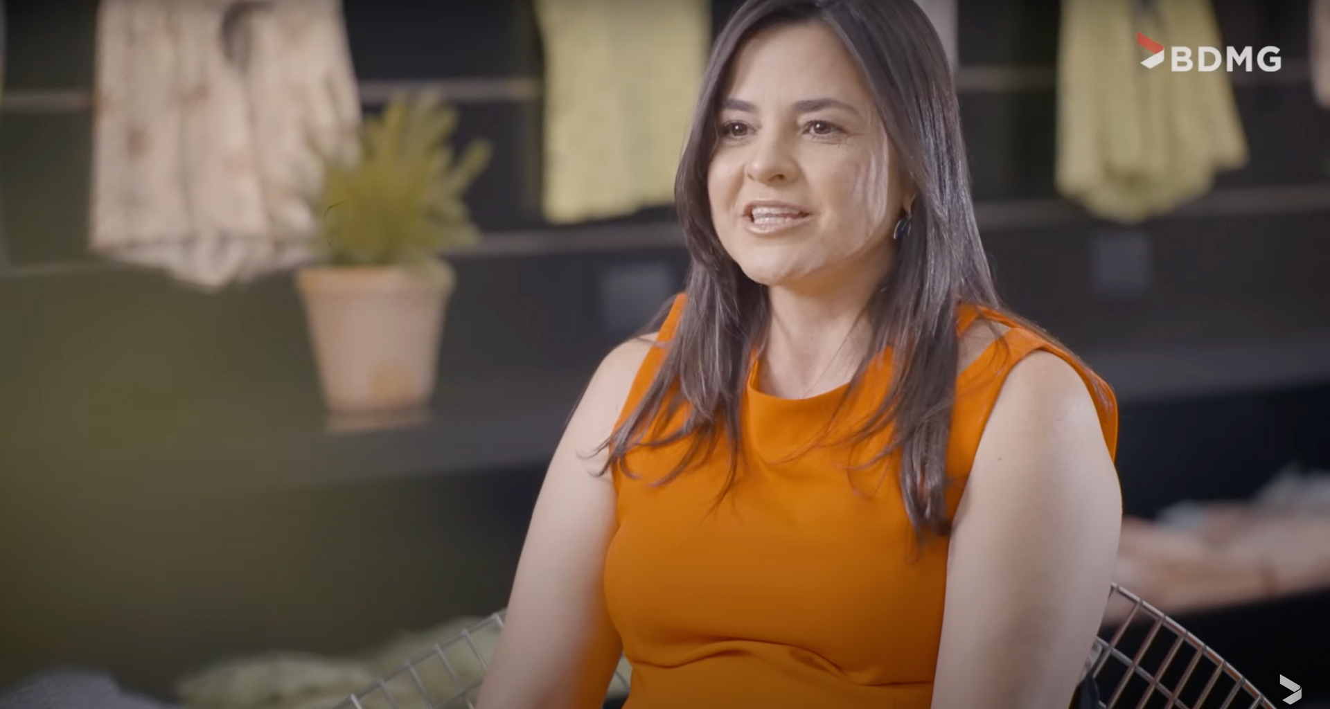 Uma mulher com um vestido laranja está sentada em um sofá conversando com alguém.