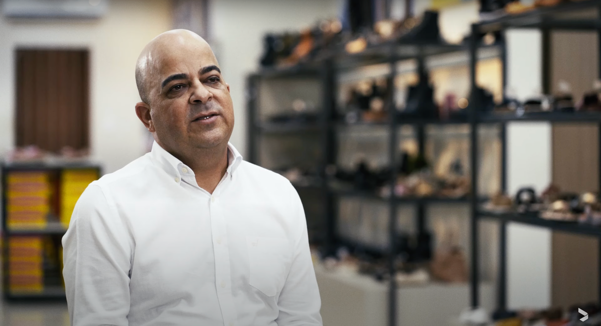 Um homem de camisa branca está sentado em frente a uma prateleira de sapatos.