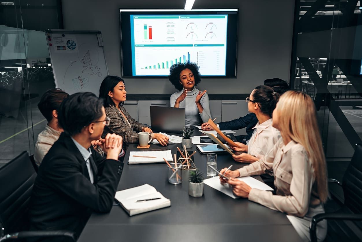 Um grupo de mulheres está sentado ao redor de uma mesa em uma reunião.