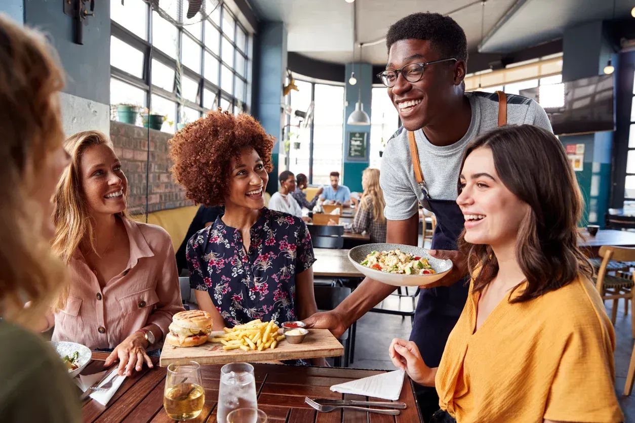Um garçom está servindo comida para um grupo de pessoas sentadas à mesa de um restaurante.