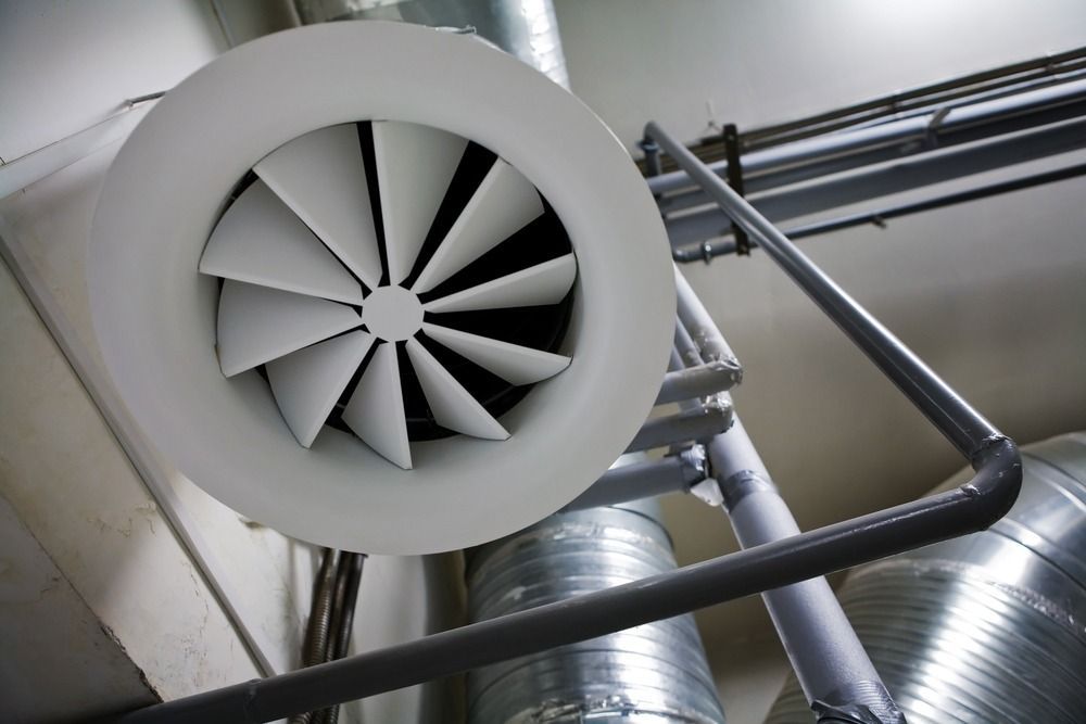 Industrial ventilation fan and metal ducts mounted on a ceiling.