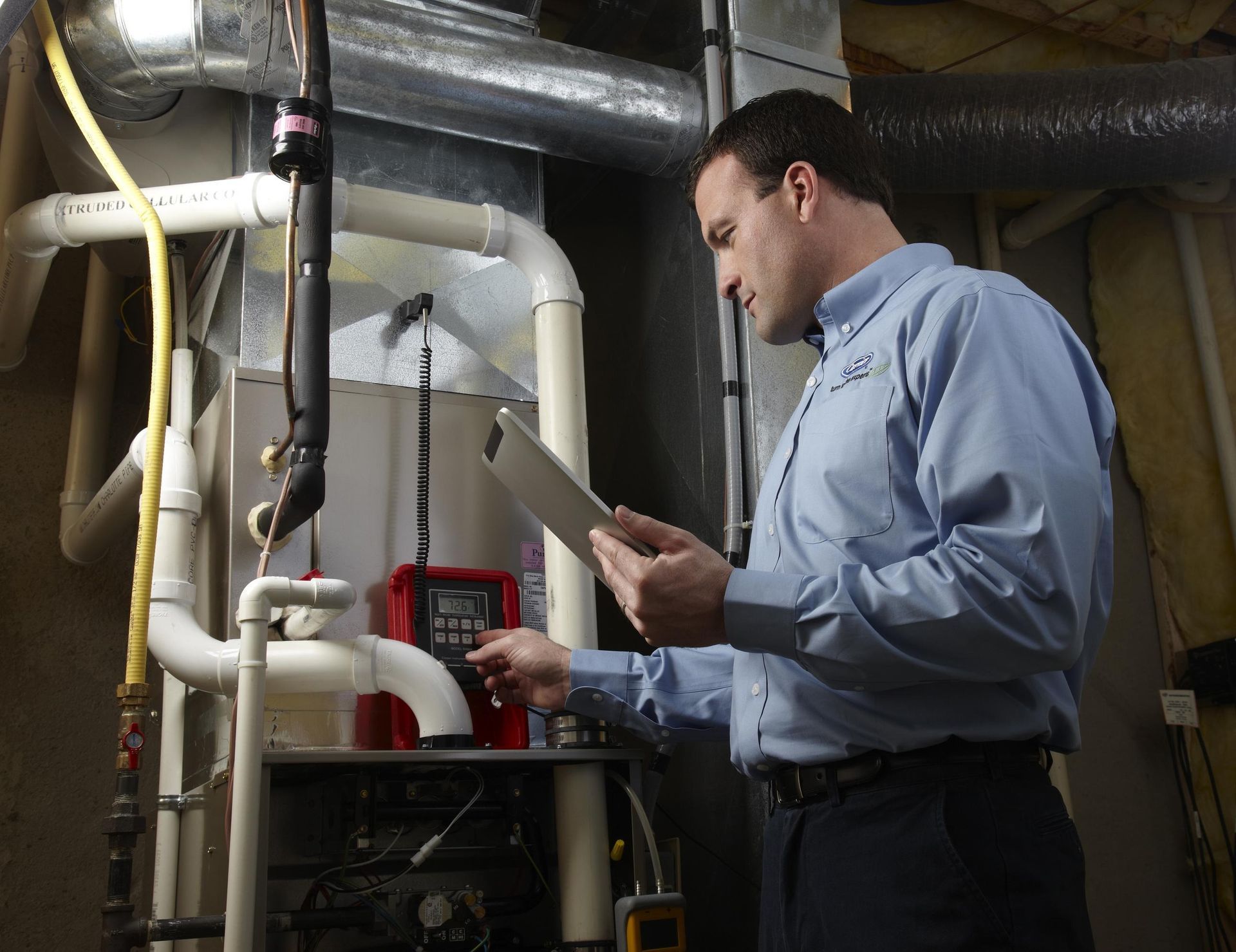 Technician inspecting HVAC equipment in a basement mechanical room with pipes and gauges