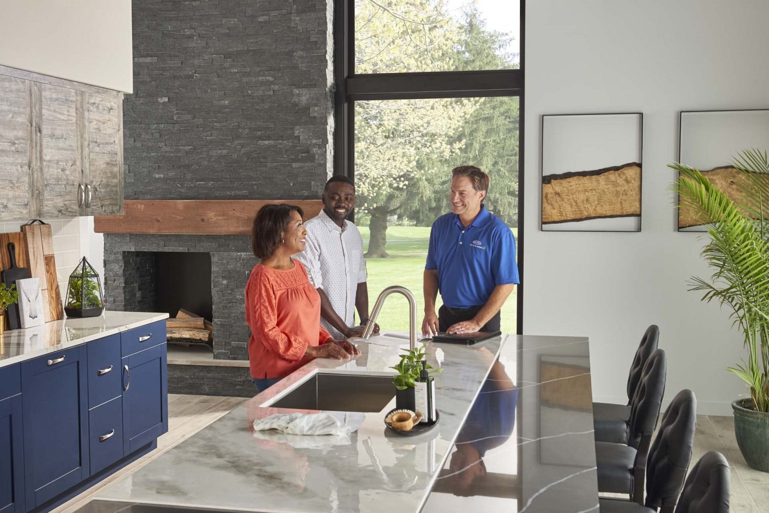 Three people talking in a modern kitchen with a marble island and large windows