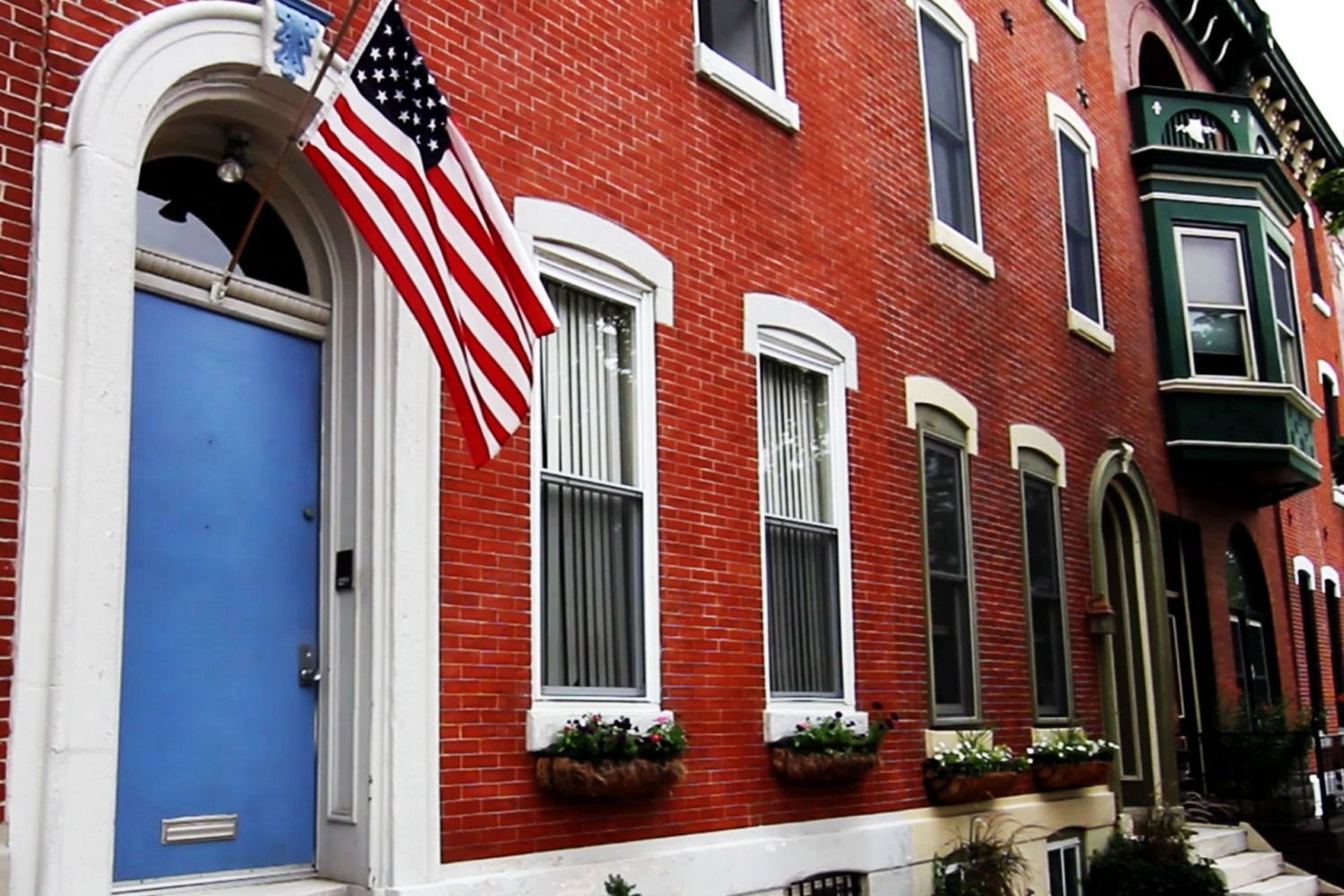 Red brick townhouse with a blue door and an American flag hanging outside.