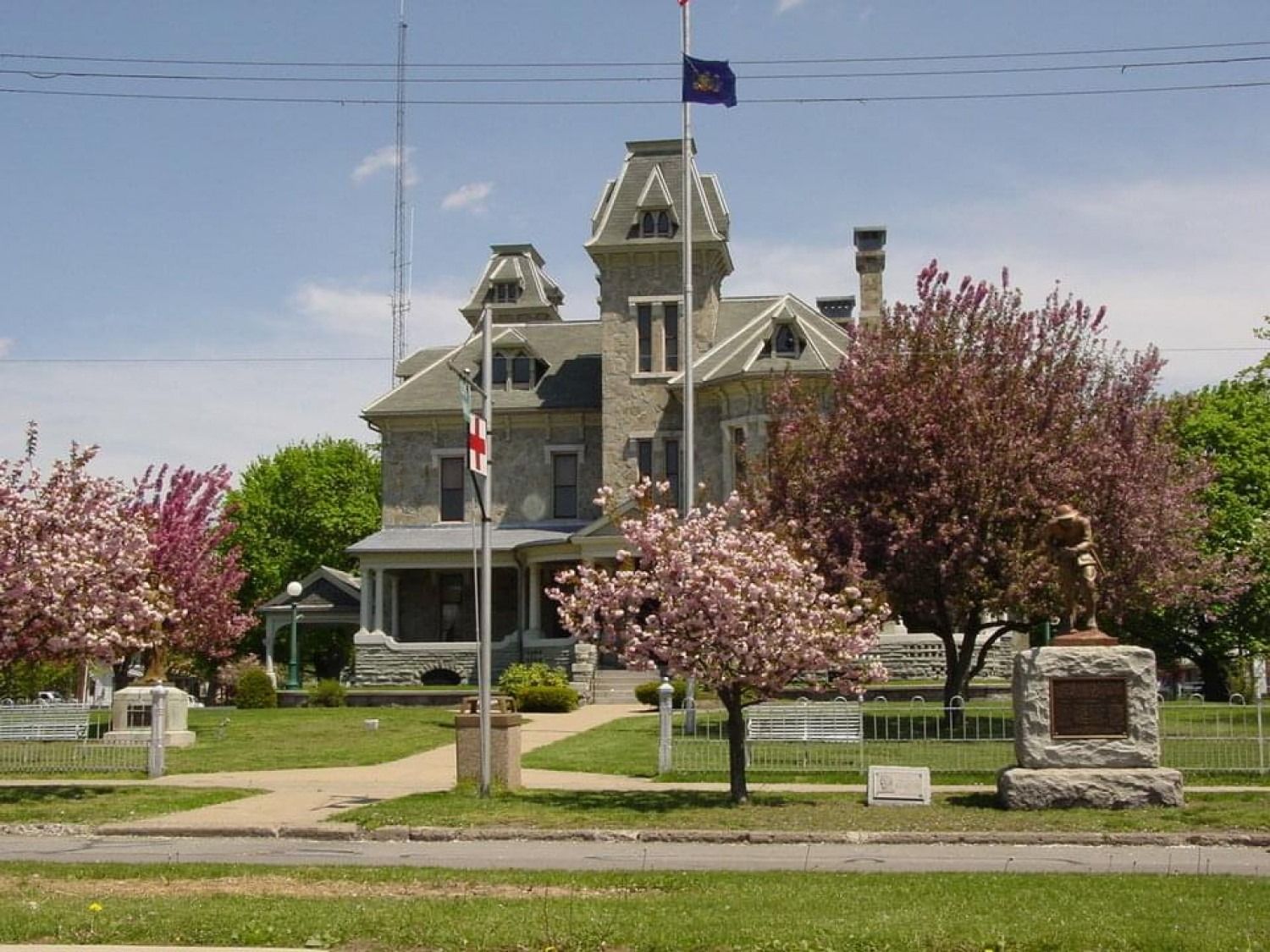 Victorian-style house with a tower, surrounded by blooming trees and a manicured lawn under a clear sky