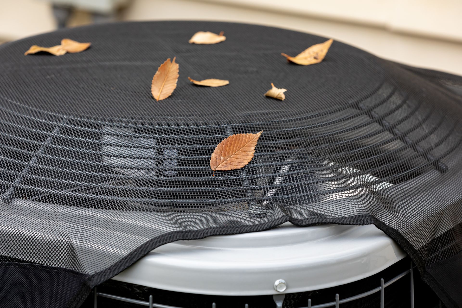 Black mesh cover over an outdoor appliance with dry leaves on top
