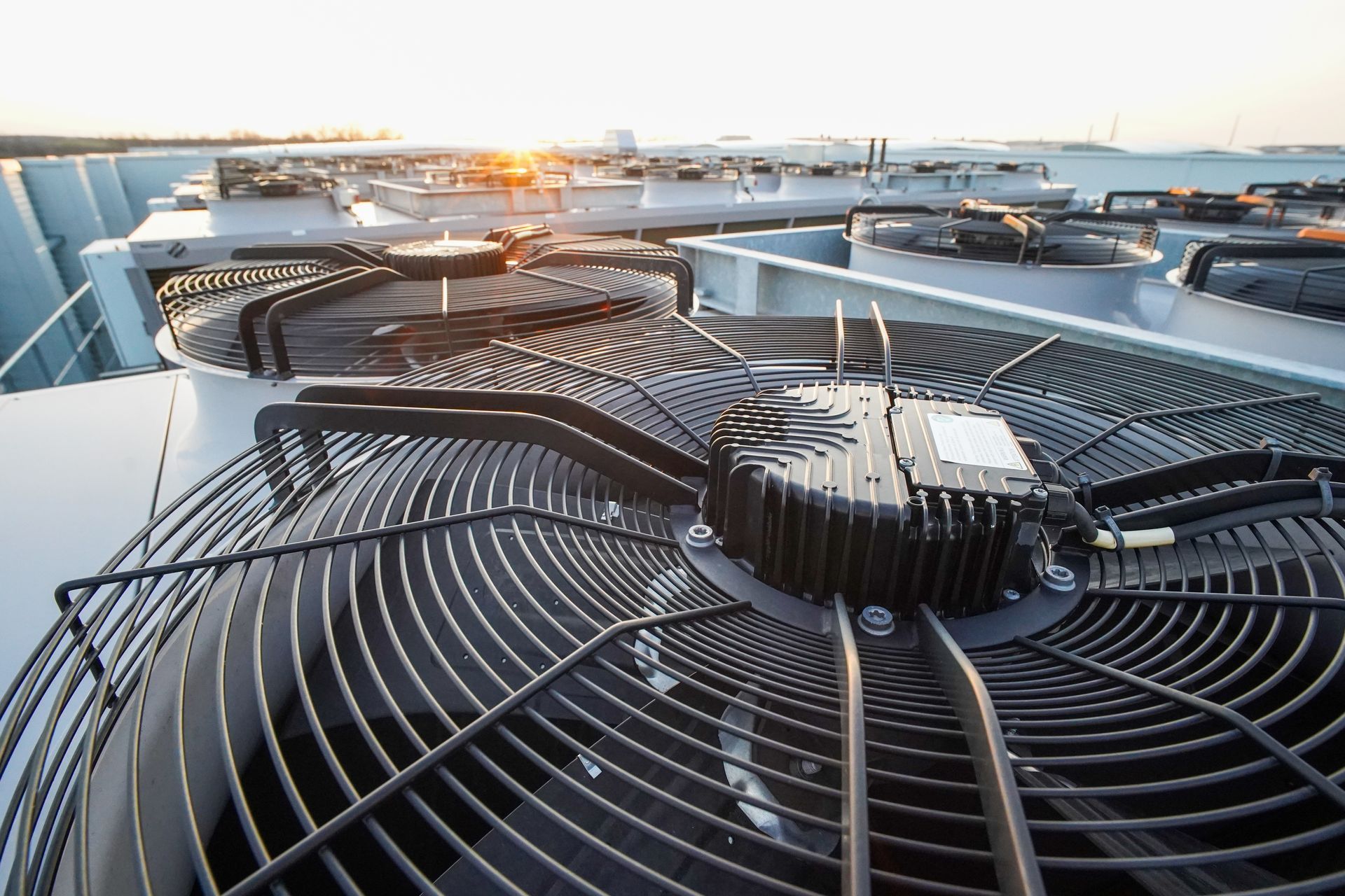 Large rooftop HVAC units with circular metal fans at sunrise.